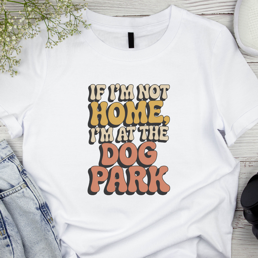 White t-shirt with 'If I'm not home, I'm at the dog park' text on a wooden surface.