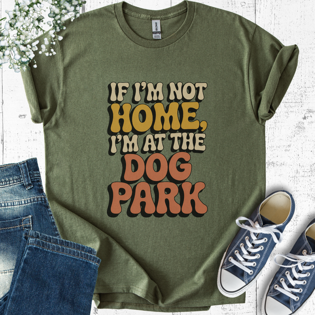 Green t-shirt with 'If I'm not home, I'm at the dog park' text, paired with jeans and sneakers on a light wooden surface.