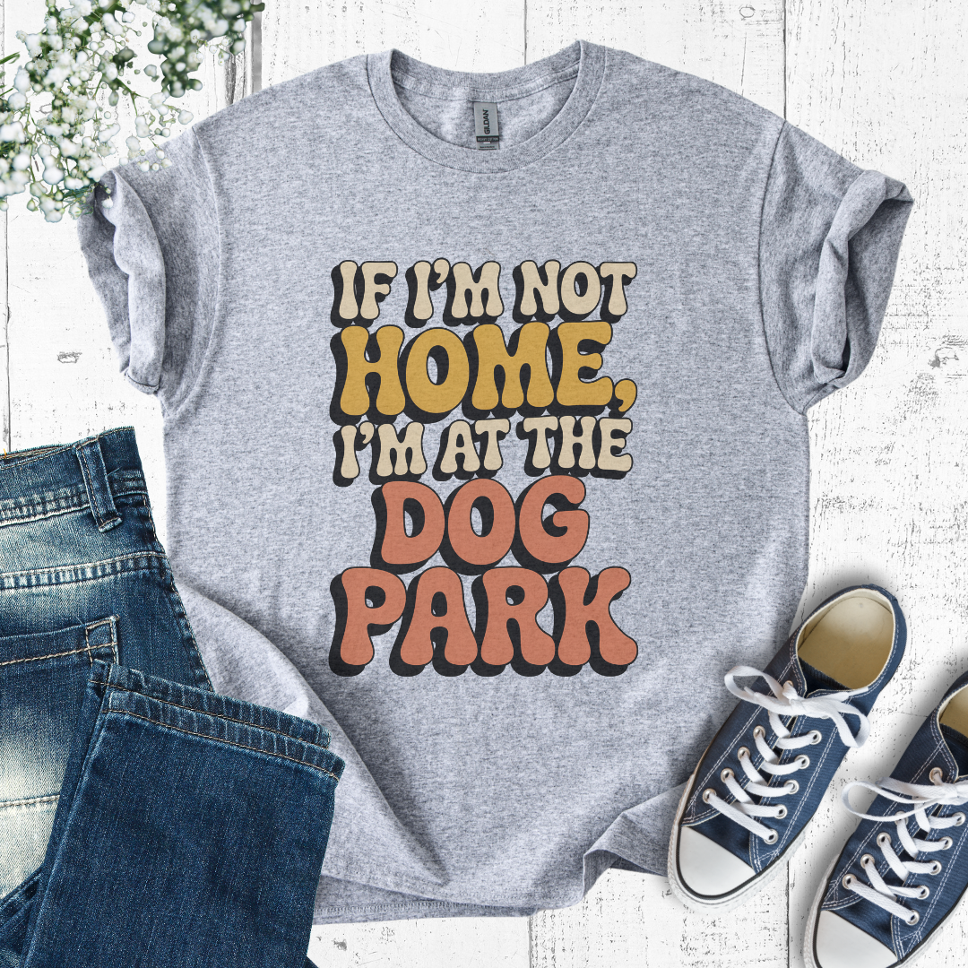 Gray t-shirt with 'If I'm not home, I'm at the dog park' text on a white background with jeans and sneakers.