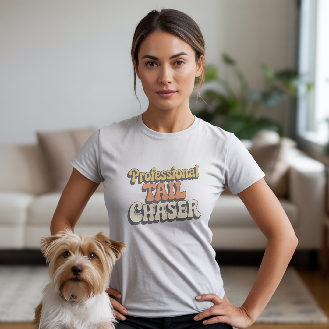 Woman wearing a 'Professional Tail Chaser' t-shirt with a dog in a living room.