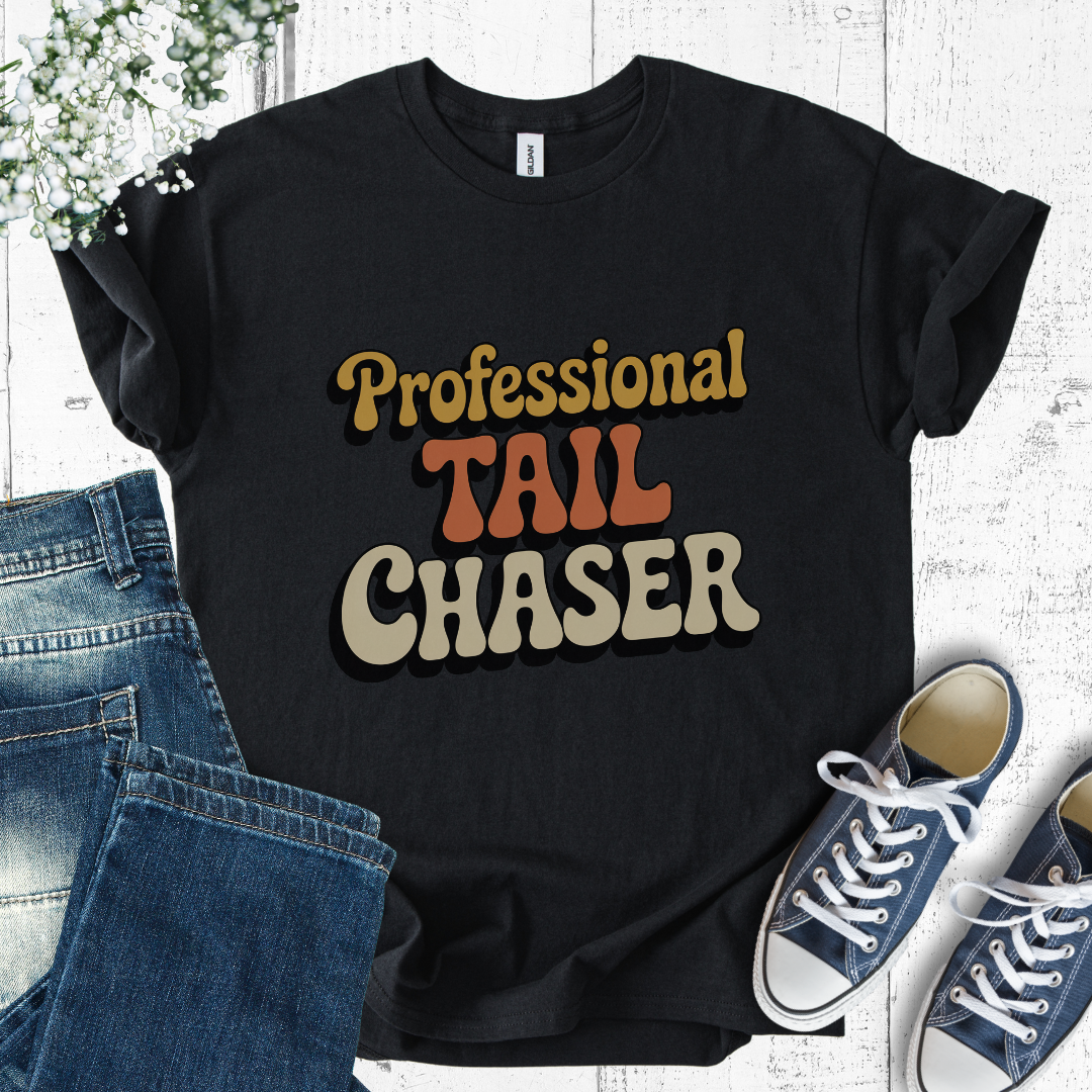Black t-shirt with 'Professional Tail Chaser' text, paired with jeans and sneakers on a light wooden surface.