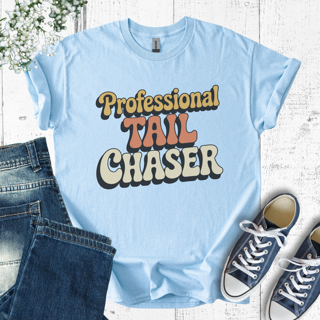 Light blue t-shirt with 'Professional Tail Chaser' text, paired with jeans and sneakers on a wooden surface.