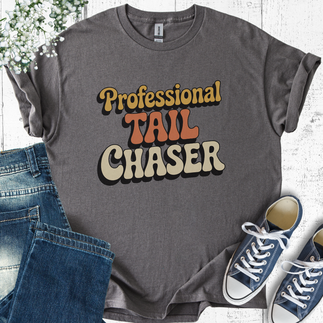 Gray t-shirt with 'Professional Tail Chaser' text, paired with jeans and sneakers on a light wooden surface.