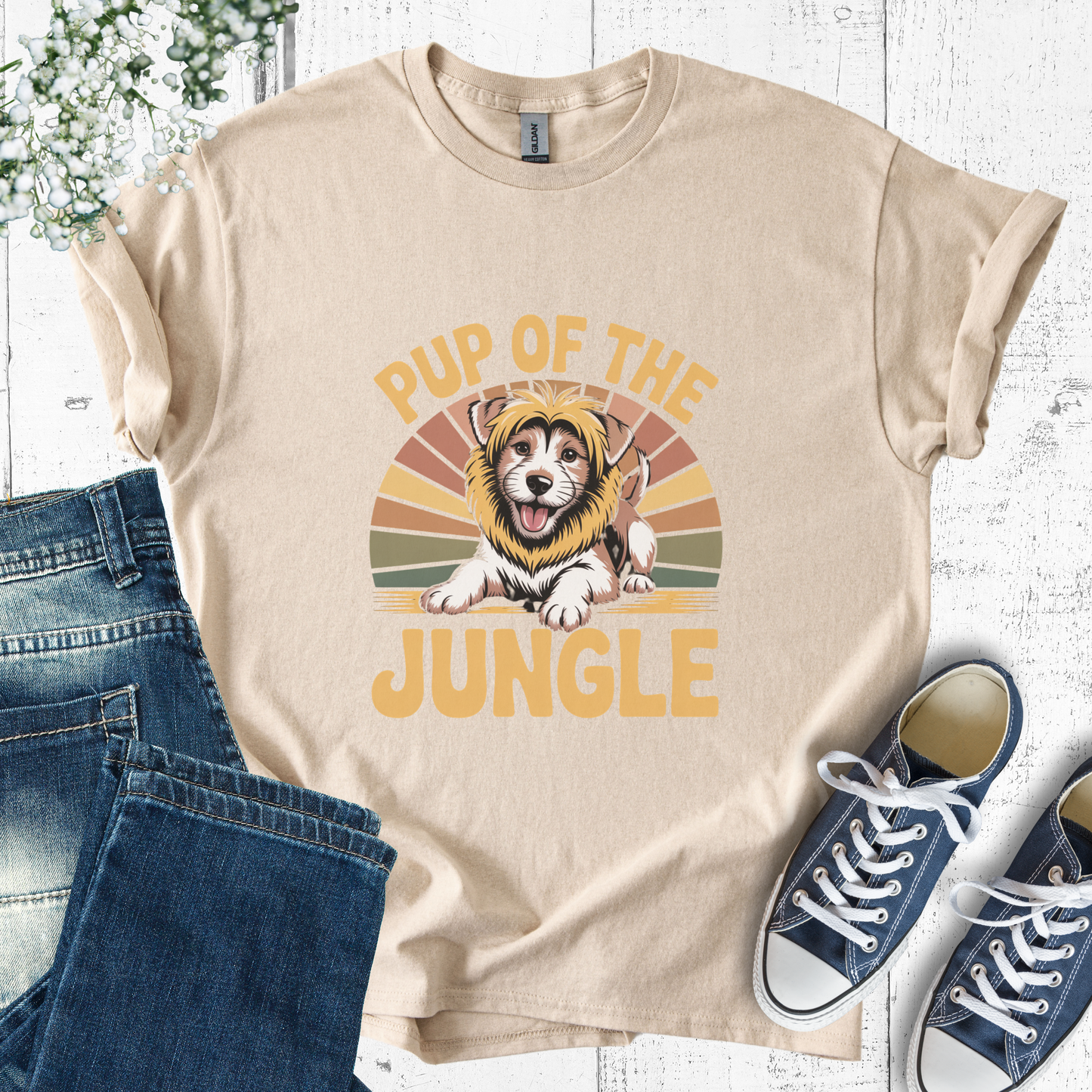 Beige t-shirt with 'Pup of the Jungle' design, blue jeans, and sneakers on a white wooden surface.