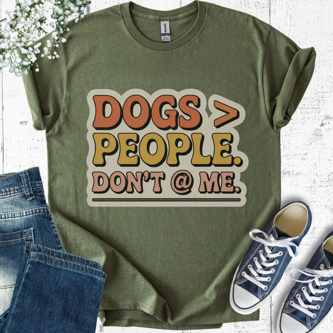 Green t-shirt with 'DOGS > PEOPLE. DON'T @ ME.' text, paired with jeans and sneakers on a light wooden surface.