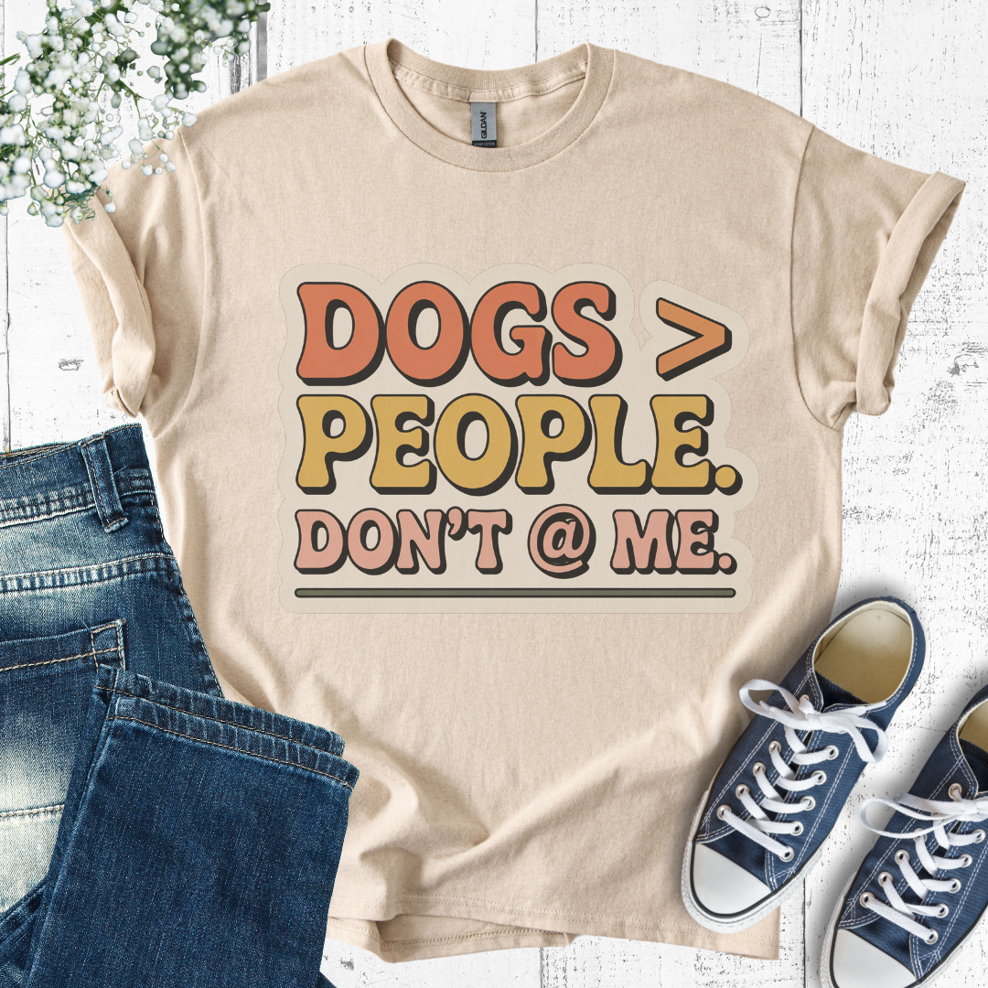 Beige t-shirt with 'DOGS > PEOPLE. DON'T @ ME.' text, paired with jeans and sneakers on a light wooden surface.