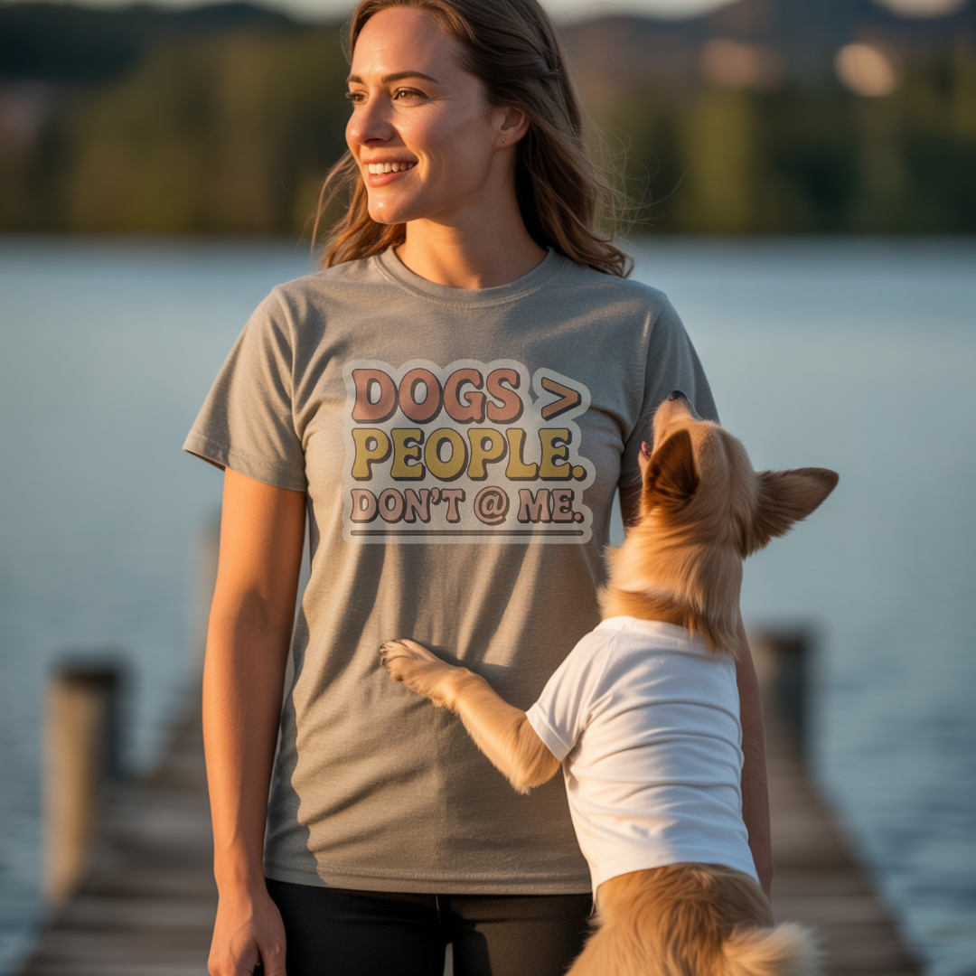 Woman wearing a t-shirt with 'DOGS > PEOPLE, DON'T @ ME.' text by a lake with a dog.