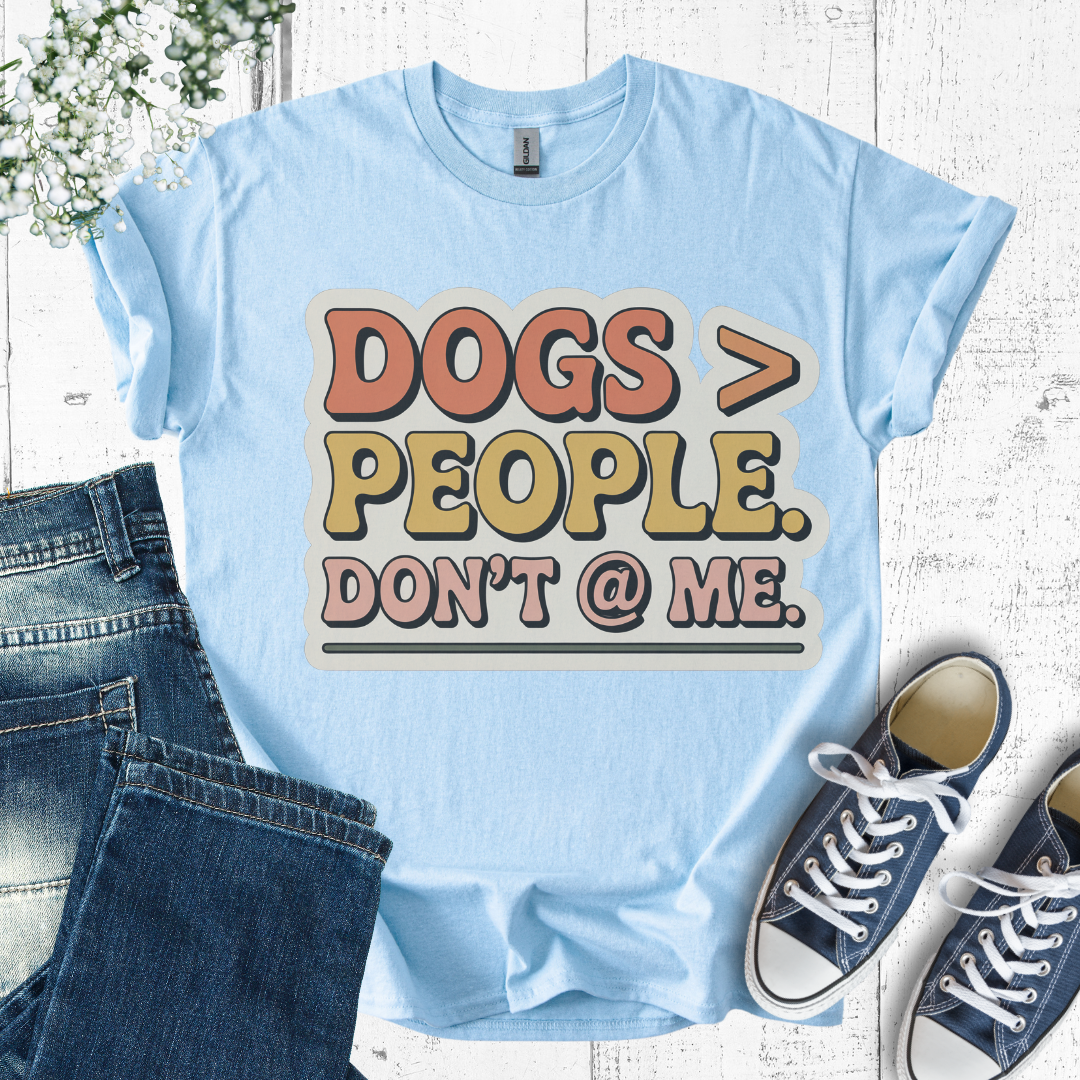 Light blue t-shirt with 'DOGS > PEOPLE. DON'T @ ME.' text, paired with jeans and sneakers on a wooden surface.