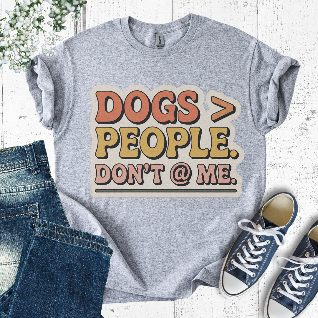 Gray t-shirt with 'DOGS > PEOPLE. DON'T @ ME.' text, paired with jeans and sneakers on a light wooden surface.