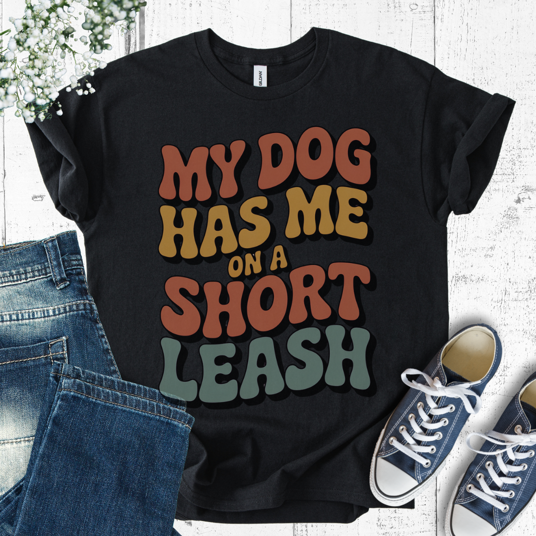 Black t-shirt with colorful text 'My dog has me on a short leash' displayed with jeans and sneakers.