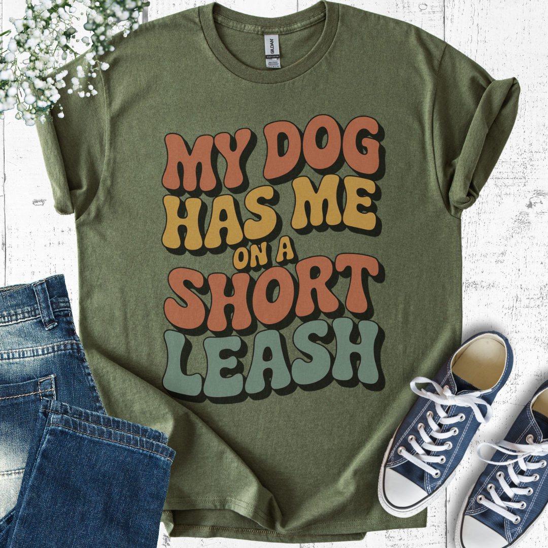 Green t-shirt with 'My dog has me on a short leash' text, paired with jeans and sneakers on a light wooden surface.