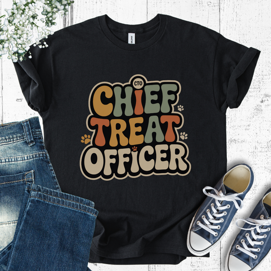 Black t-shirt with 'Chief Treat Officer' text, jeans, and sneakers on a light wooden surface.