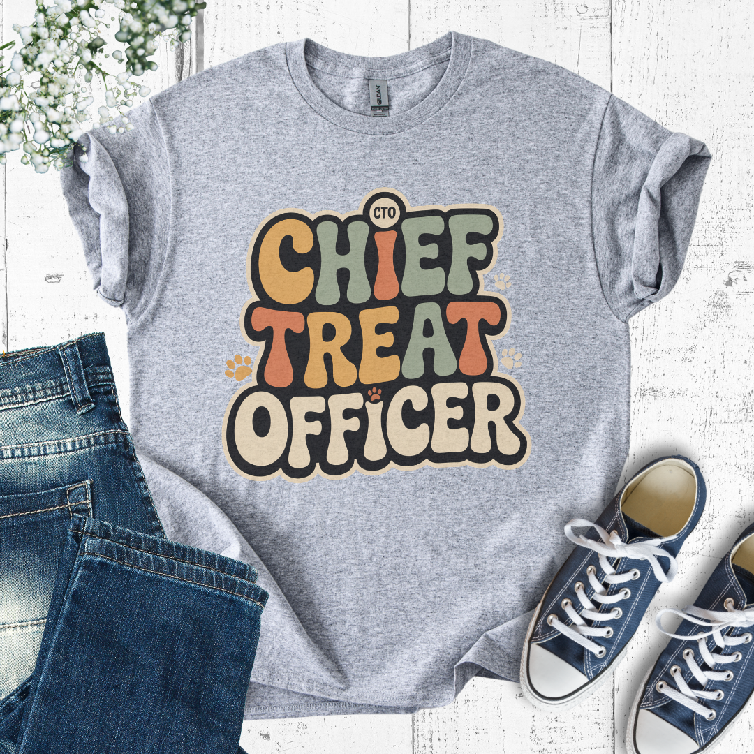 Gray t-shirt with 'Chief Treat Officer' text, paired with jeans and sneakers on a light wooden surface.