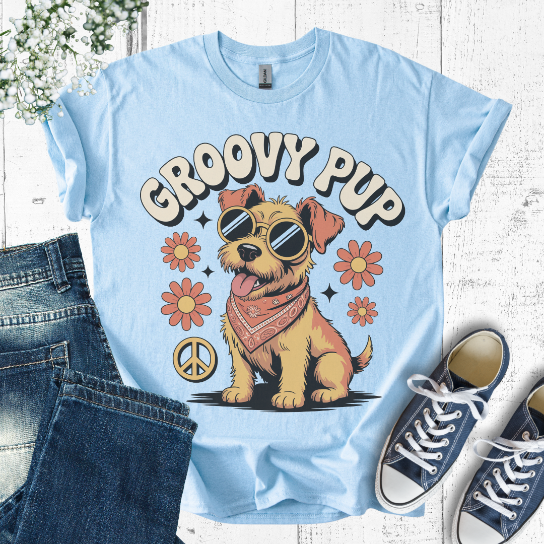 Light blue t-shirt with 'Groovy Pup' design featuring a dog wearing sunglasses and a bandana, paired with jeans and sneakers on a wooden surface.