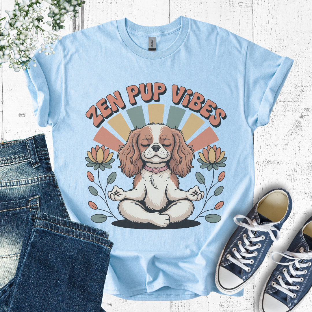 Light blue t-shirt with 'Zen Pup Vibes' design featuring a dog in a meditative pose, placed on a wooden surface with jeans and sneakers.