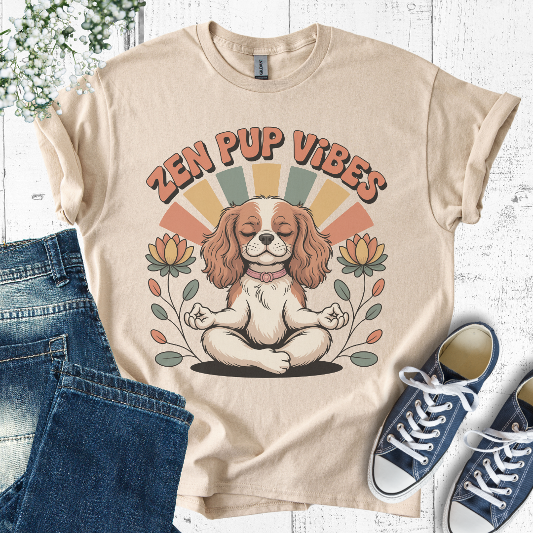 Beige t-shirt with 'Zen Pup Vibes' design featuring a dog in a meditative pose, placed on a white wooden surface with jeans and sneakers.