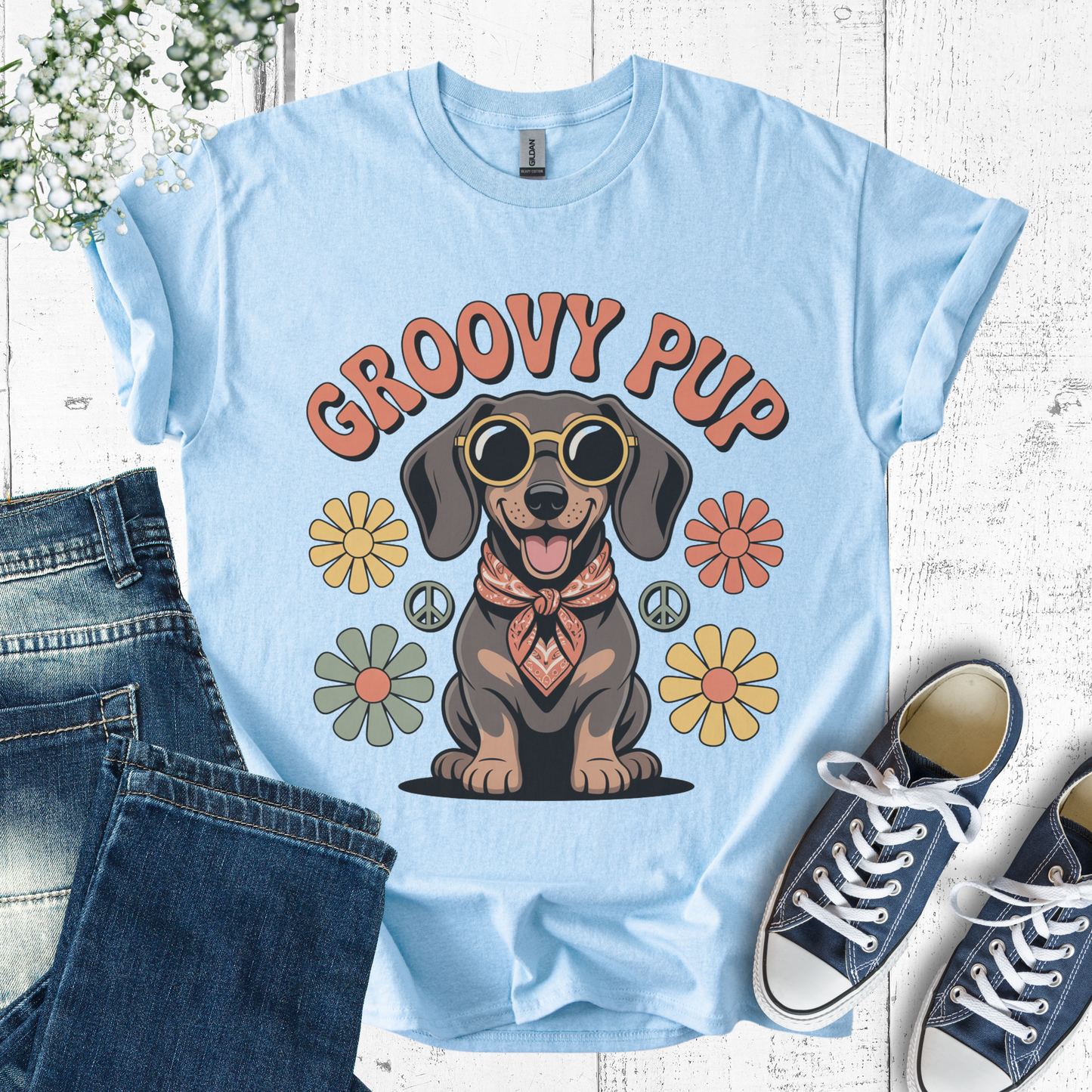 Light blue t-shirt with 'Groovy Pup' design featuring a dog, flowers, and peace signs, displayed with jeans and sneakers.