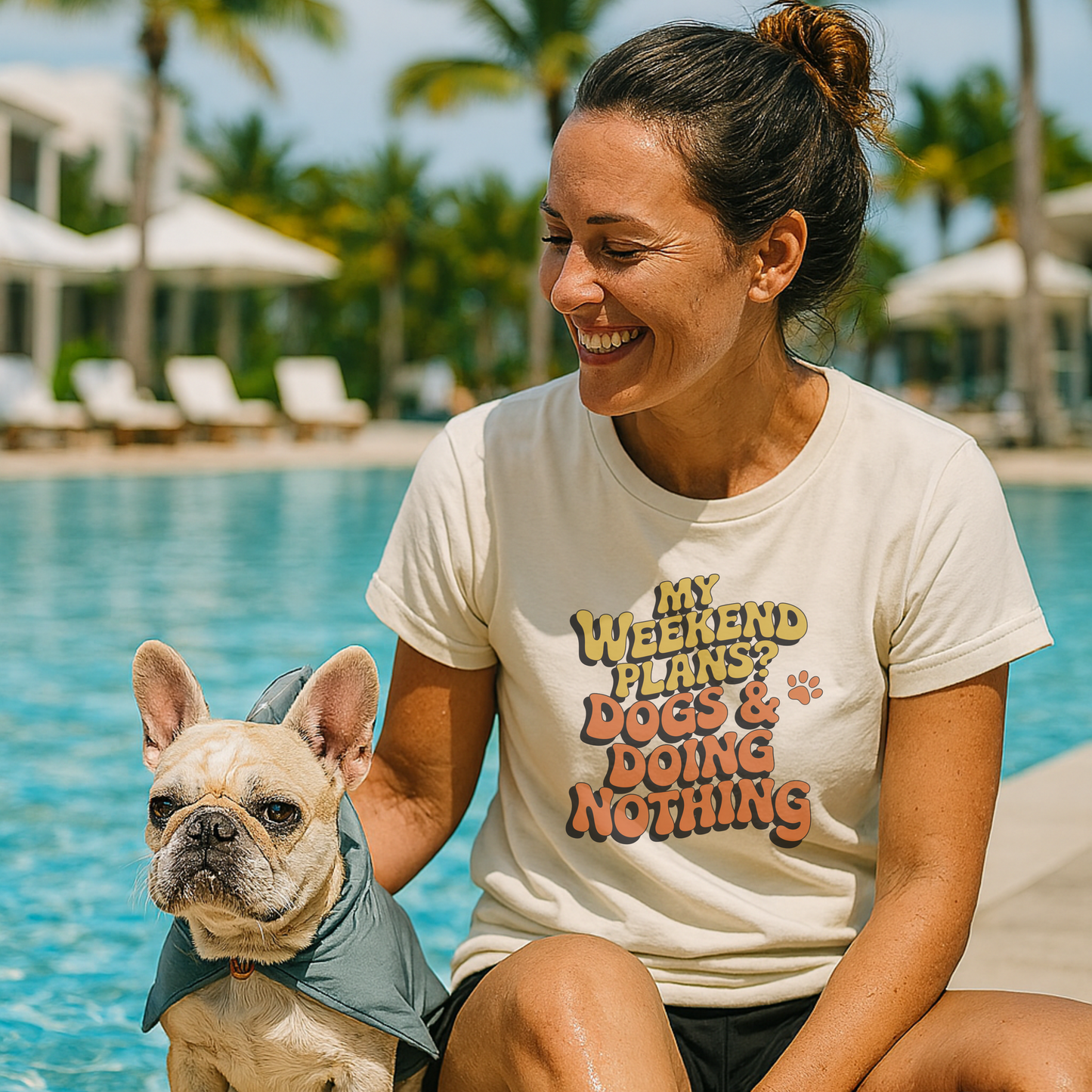 Woman sitting by a pool with a dog, wearing a t-shirt with text.