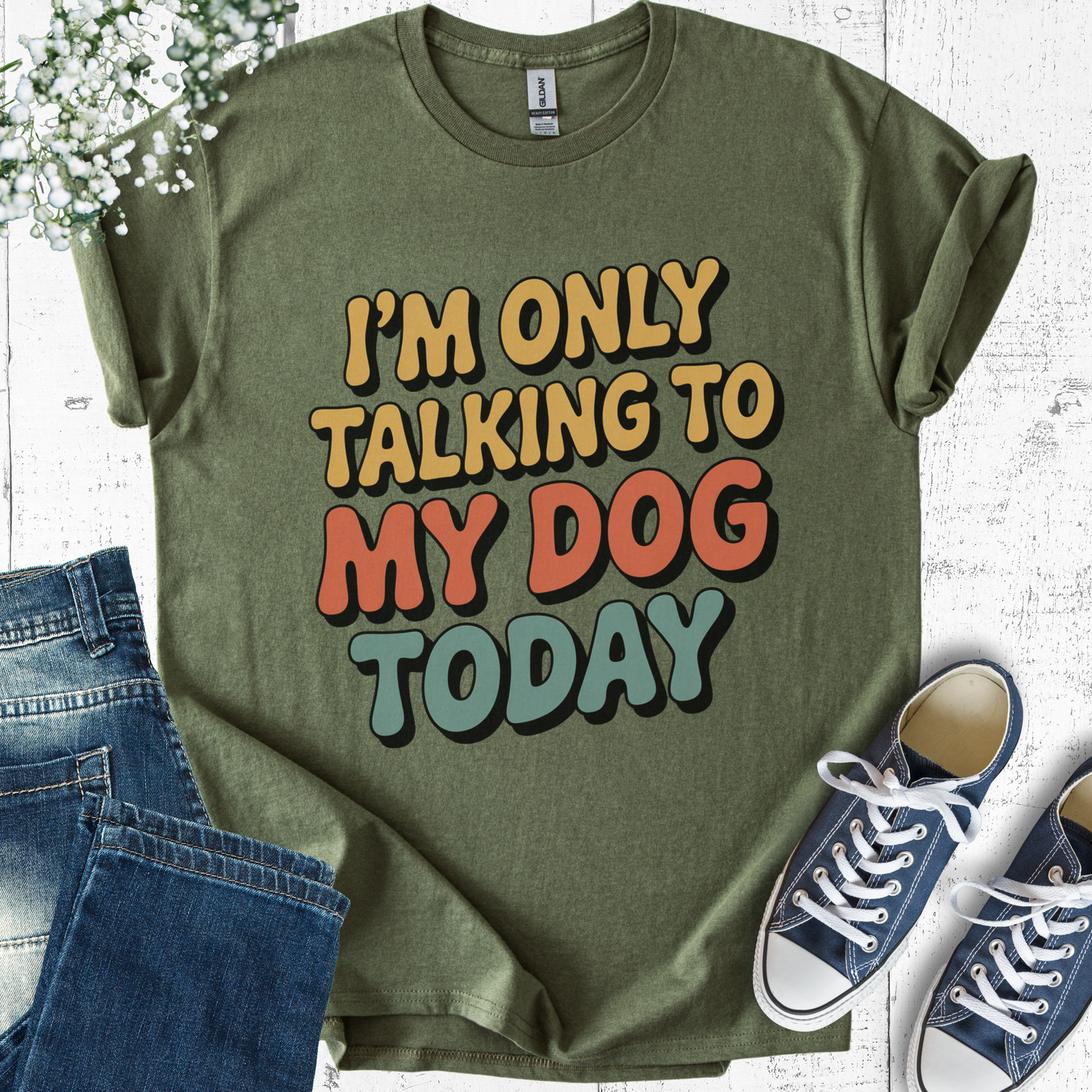 Green t-shirt with 'I'm only talking to my dog today' text, paired with jeans and sneakers on a light wooden surface.