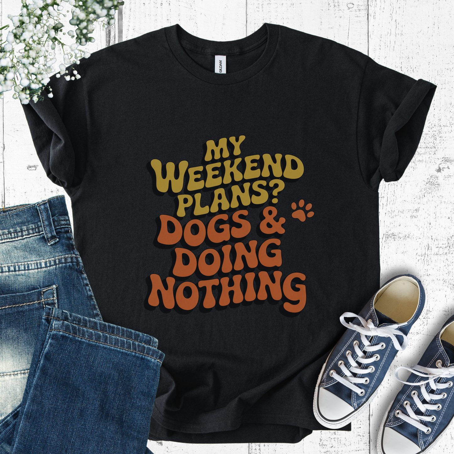 Black t-shirt with 'My weekend plans? Dogs & doing nothing' text, paired with jeans and sneakers on a light background.