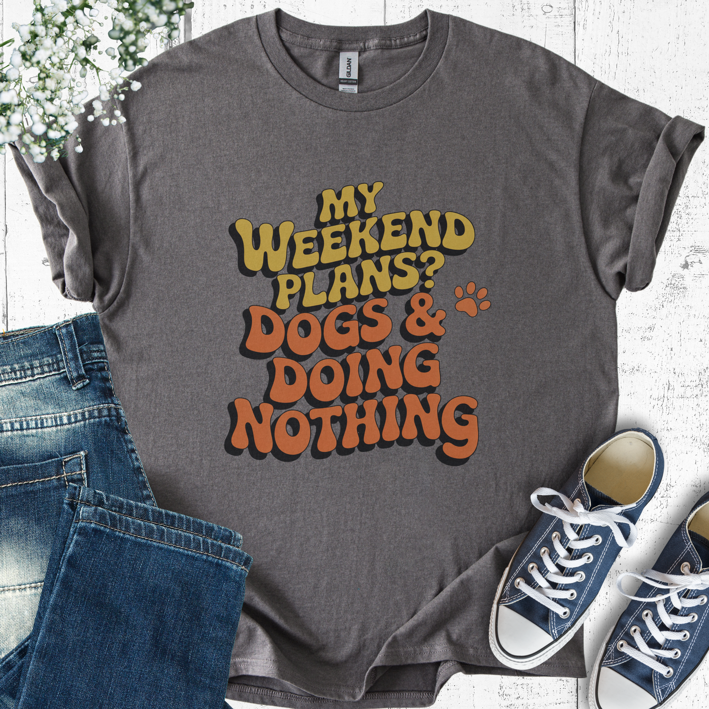 Gray t-shirt with 'My weekend plans? Dogs & doing nothing' text, paired with jeans and sneakers on a light wooden surface.