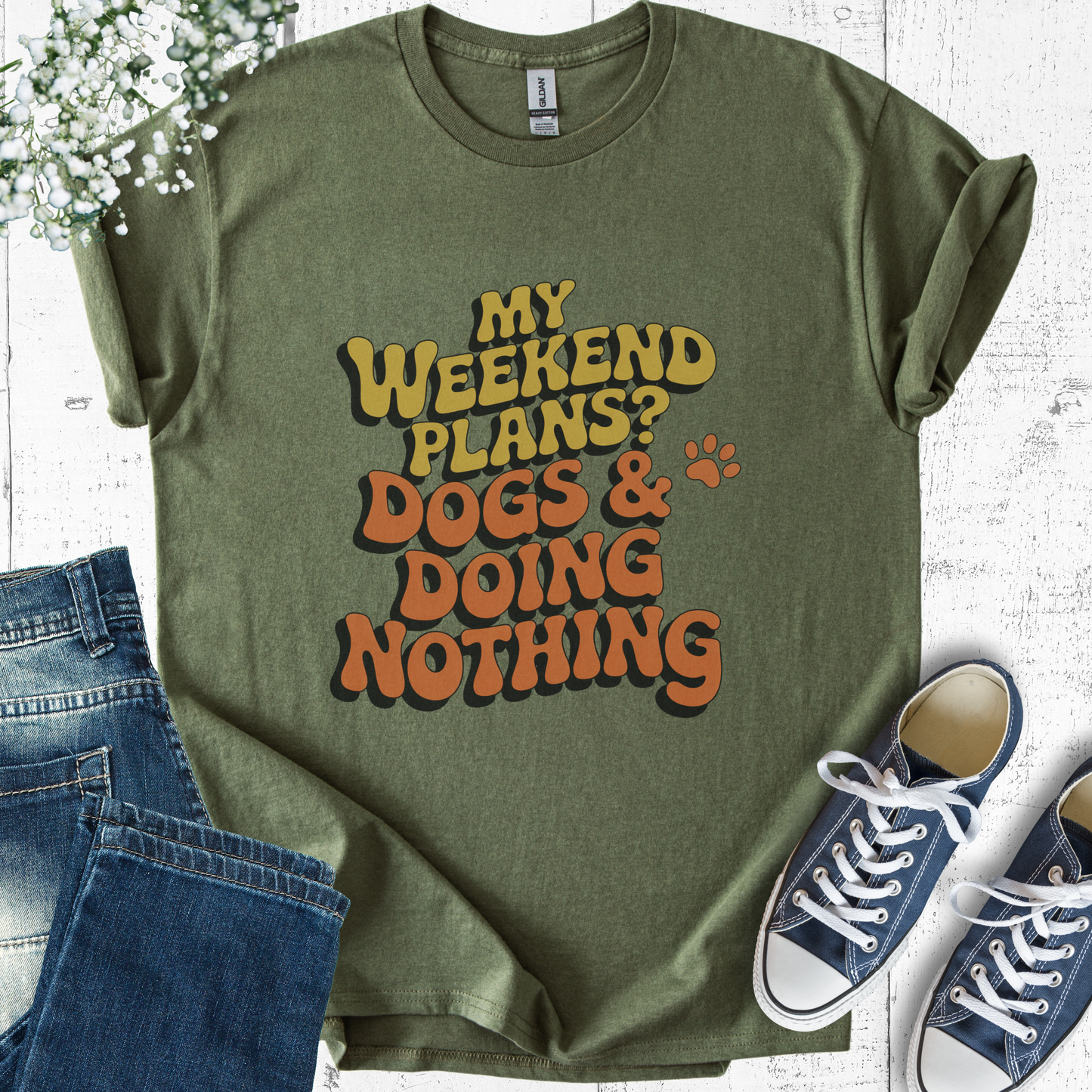 Green t-shirt with 'My weekend plans? Dogs & doing nothing' text, paired with jeans and sneakers on a light wooden surface.