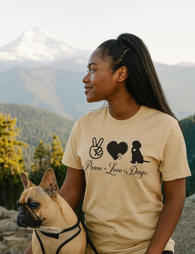 Woman wearing a beige t-shirt with a dog graphic and text, standing outdoors with mountains in the background.
