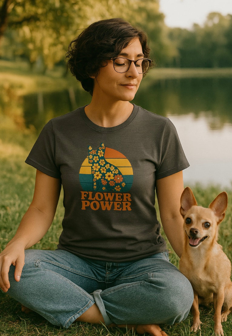 Person wearing a 'Flower Power' t-shirt sitting on grass with a dog.