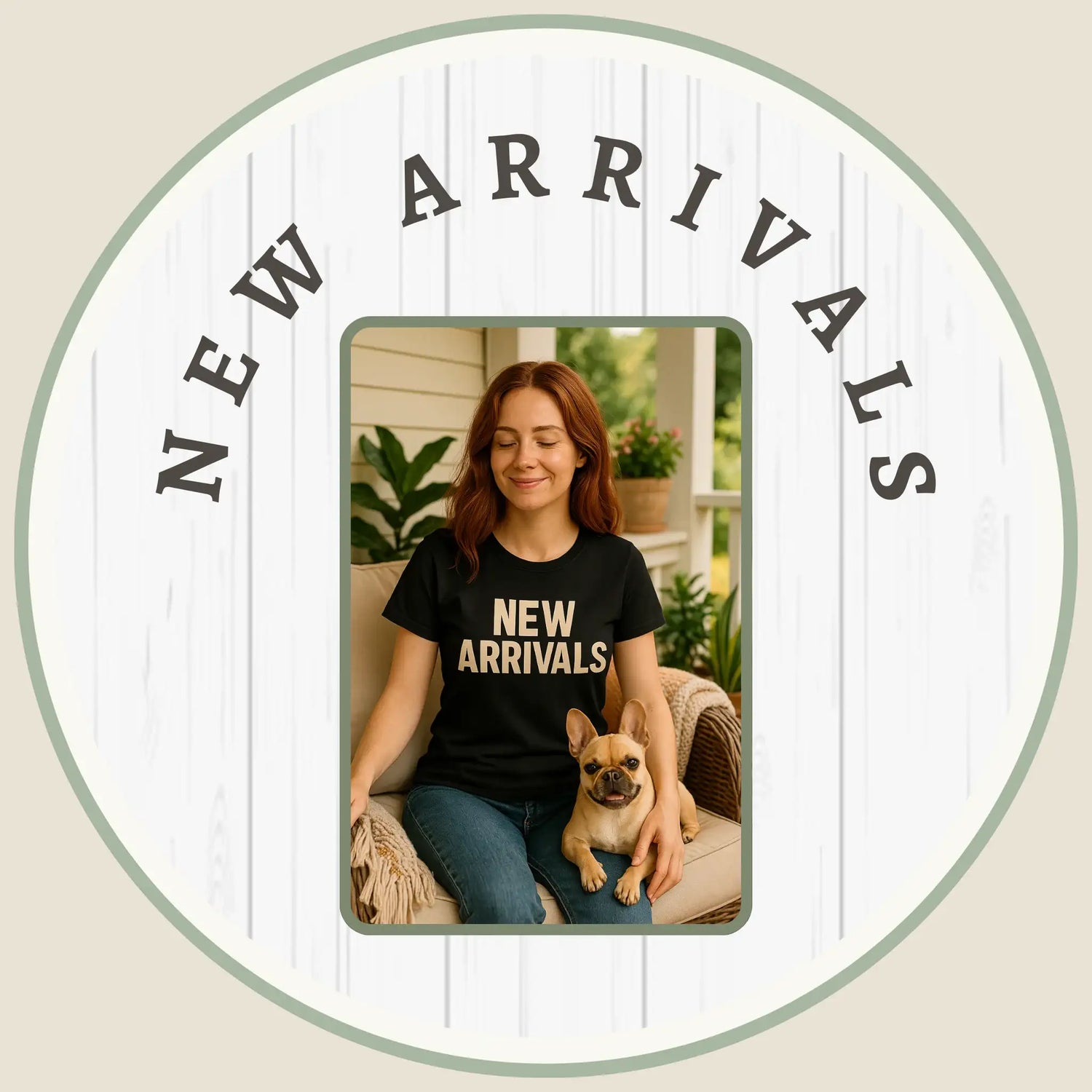 A happy woman with long auburn hair sits on a porch wearing a black t-shirt that says "NEW ARRIVALS" with her dog beside her.
