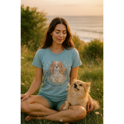 Woman sitting in a field with a dog, wearing a blue t-shirt with a dog illustration.