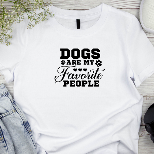 White t-shirt with 'Dogs are my favorite people' text on a wooden surface with denim jeans and flowers.