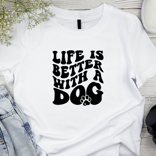 White t-shirt with 'Life is better with a dog' text on a wooden surface.