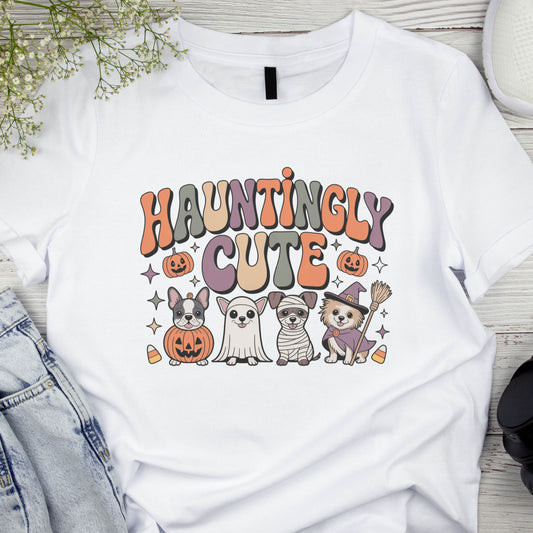 White t-shirt with 'Hauntingly Cute' text and Halloween-themed graphics on a wooden surface.