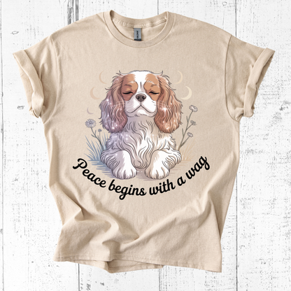 Beige t-shirt with a dog illustration and 'Peace begins with a wag' text on a wooden surface