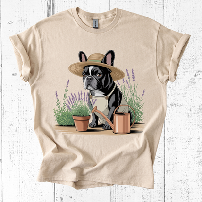 Beige t-shirt with a dog wearing a hat and holding a watering can graphic on a white wooden background