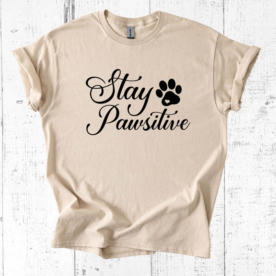 Beige t-shirt with 'Stay Pawsitive' text and paw print on a white wooden background