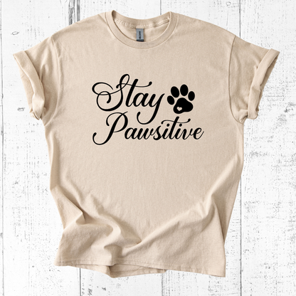 Beige t-shirt with 'Stay Pawsitive' text and paw print on a white wooden background