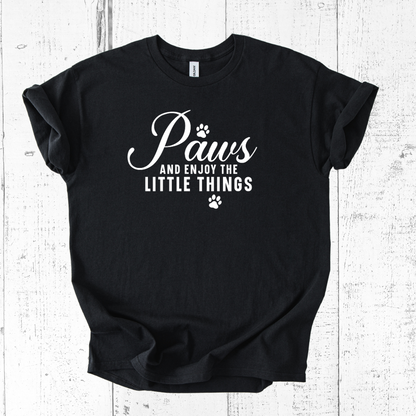 Black t-shirt with white text 'Paws and enjoy the little things' on a wooden surface