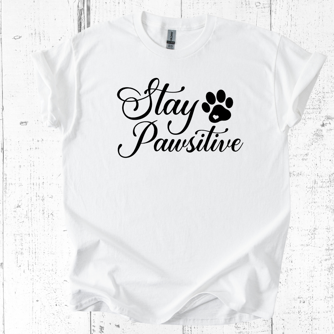 White t-shirt with 'Stay Pawsitive' text and paw print on a wooden surface