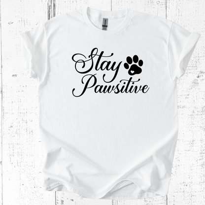 White t-shirt with 'Stay Pawsitive' text and paw print on a wooden surface