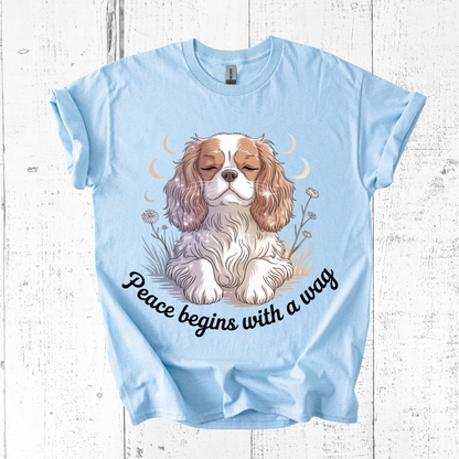 Light blue t-shirt with a dog graphic and 'Peace begins with a wag' text on a wooden surface.