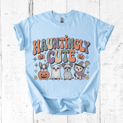 Light blue t-shirt with 'Hauntingly Cute' text and Halloween-themed graphics on a wooden surface.