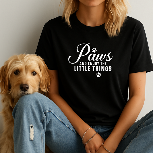 Person wearing a black t-shirt with 'Paws and enjoy the little things' text sitting next to a dog.