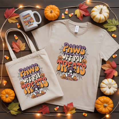 T-shirt and tote bag with 'Paws Off My Treats' design on a wooden surface with pumpkins and leaves.