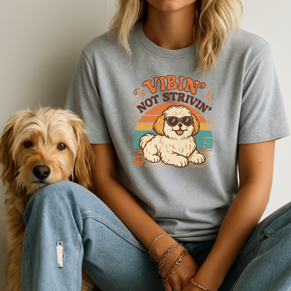 Person wearing a t-shirt with a dog graphic and text, sitting next to a dog. 'Vibin' Not Strivin'.