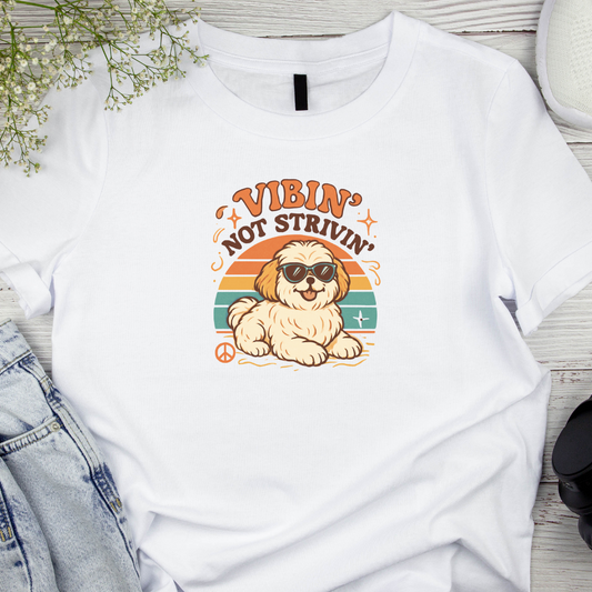 White T-Shirt on a wooden background with a graphic and text saying 'Vibin Not Strivin'.