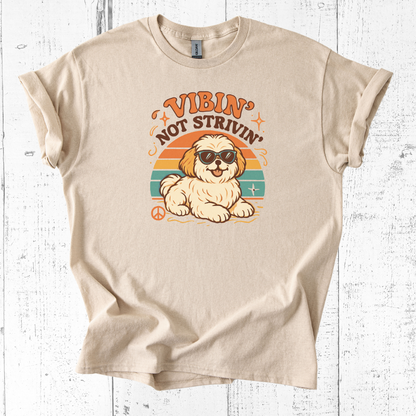 Beige T-Shirt with small dog graphic wearing sunglasses and retro sunset background with text saying "Vibin' Not Strivin'.