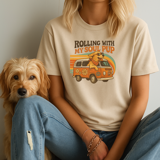 Person wearing a t-shirt with a graphic of a dog and van, sitting next to a small dog.