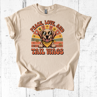 Beige t-shirt with a graphic of a dog and text 'Peace Love and Tail Wags' on a wooden surface.