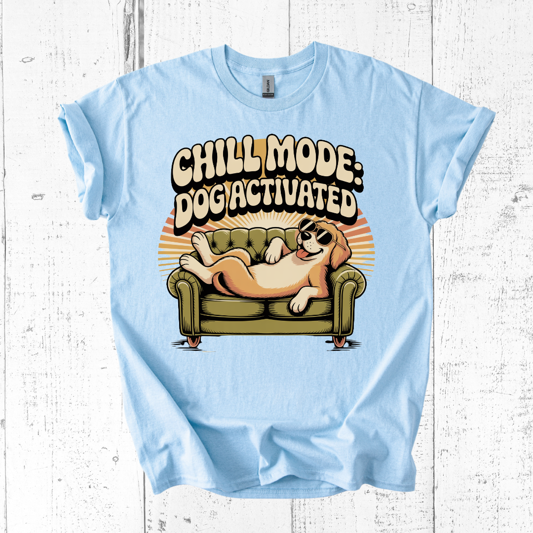 Light blue t-shirt with a dog on a couch graphic and 'Chill Mode: Dogactivated' text on a white wooden background.